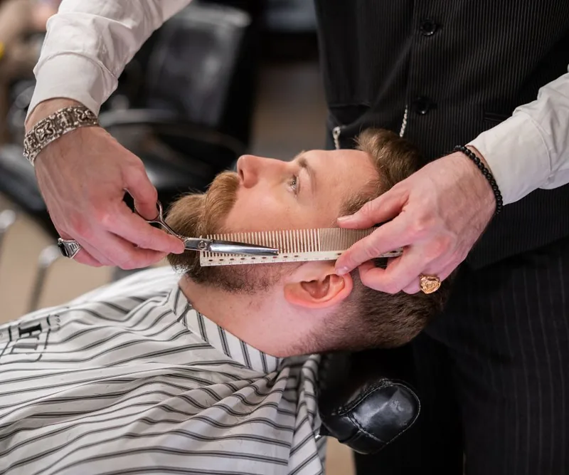 Detalle de un barbero perfilando una barba con tijeras y peine